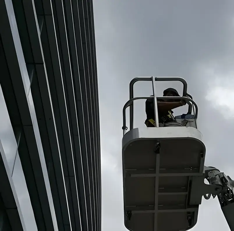 Technician in an aerial-lift basket beside a louvred facade