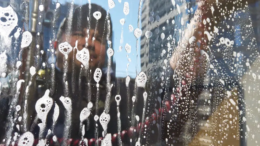 Suds on a pane mid-wash, a technician behind the glass